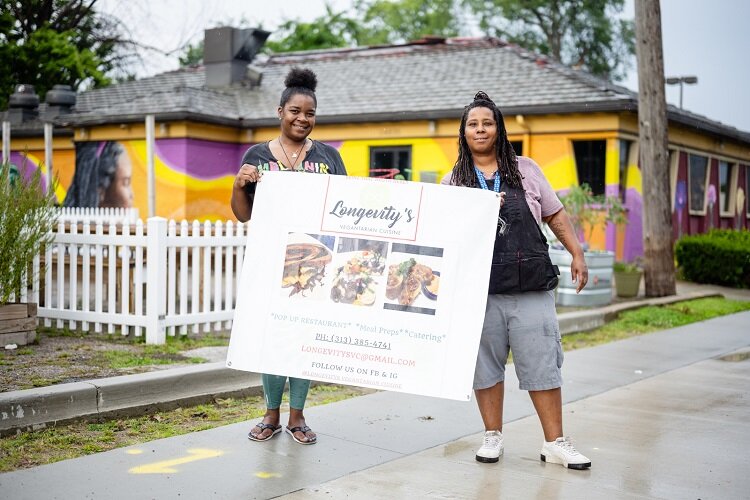 Cawana and Nina Bradford of Longevity's Vegetarian cuisine hold up a sign advertising their business.