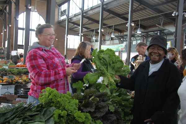 Becky of Beilait Farms hands kale to Ethel Ambrols of Brush Park Manor