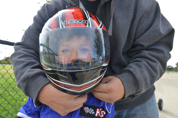 A young racer's father helps him with his helmet