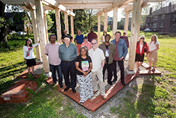Myrtle Thompson, center, Program Director and Co-Founder of Feedum Freedom, and Mikel Bresee, right center, pose with community members in front of a pavilion being built as part of the Fox Creek Artscape.