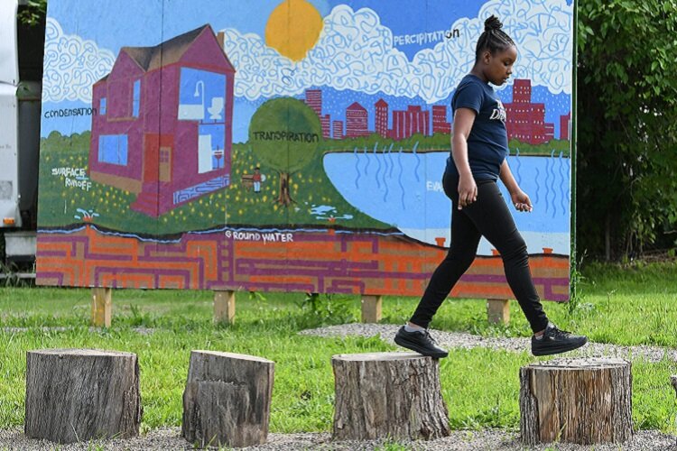 A young neighborhood resident has some fun in front of a water cycle mural at the Hamilton Rainscape Learning Lab.