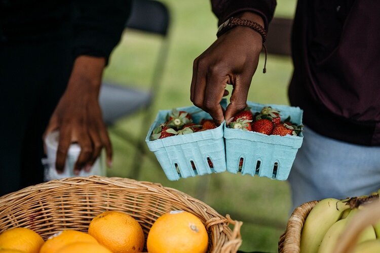 A farm stand worker picks up some cartons of strawberries.