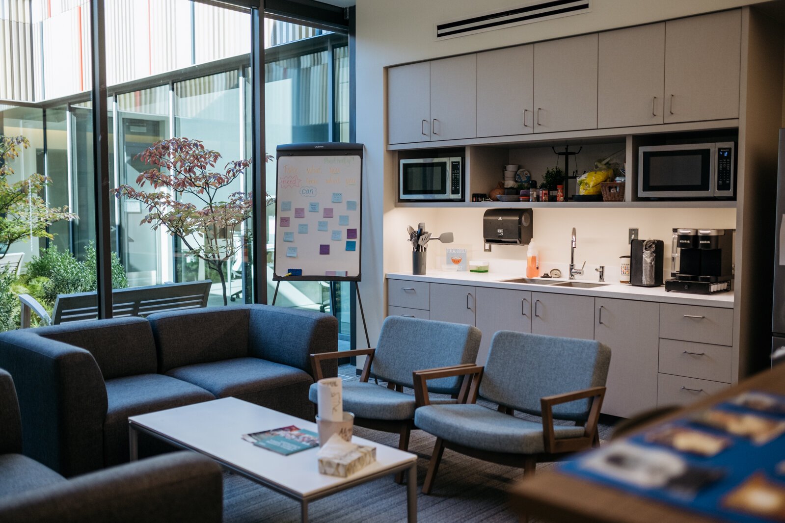 The staff wellness lounge sports healthy snacks, coffee, yoga on TV, and space for eating, relaxing, or finishing a project. The adjacent atrium encourages teachers to rest in sunshine and nature.