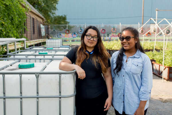 Kandis Chow and Brianna Bryant posing with the water tanks for the irrigation system The Mercy Midnight Storm is designing.