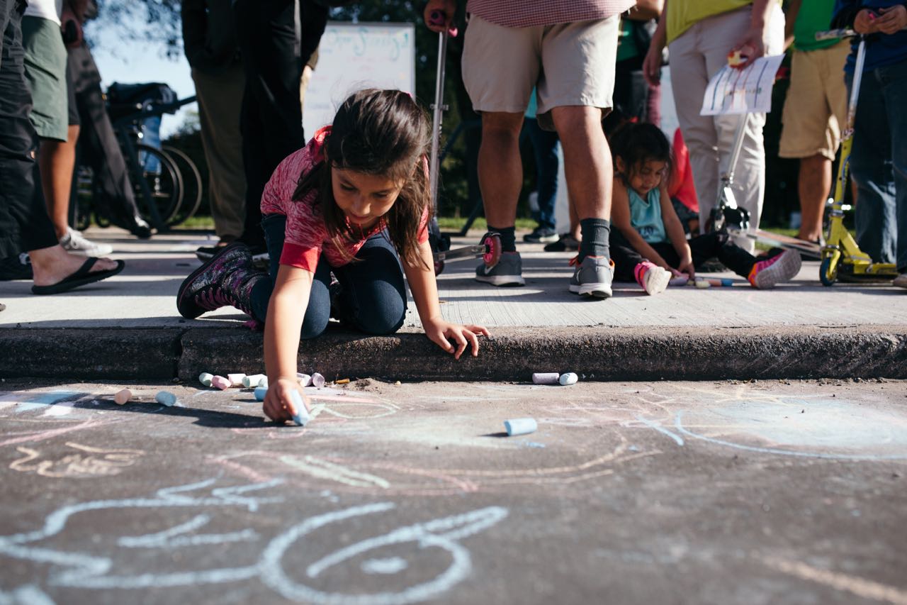 A girl writes on the street in chalk during Open Streets Detroit
