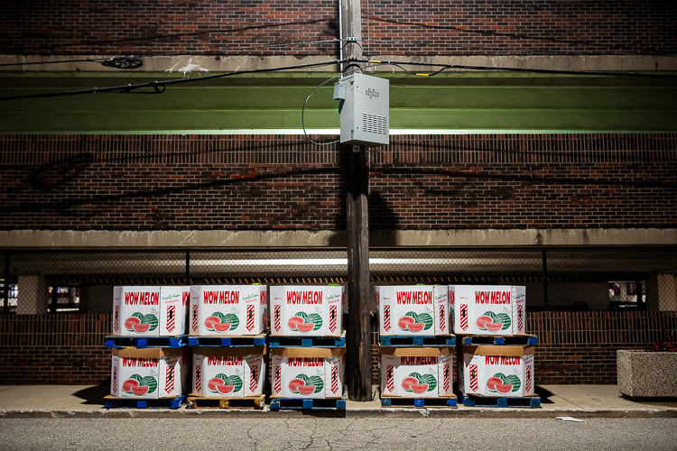Boxes of watermelons lined up against the parking structure across from Shed 3's parking lot