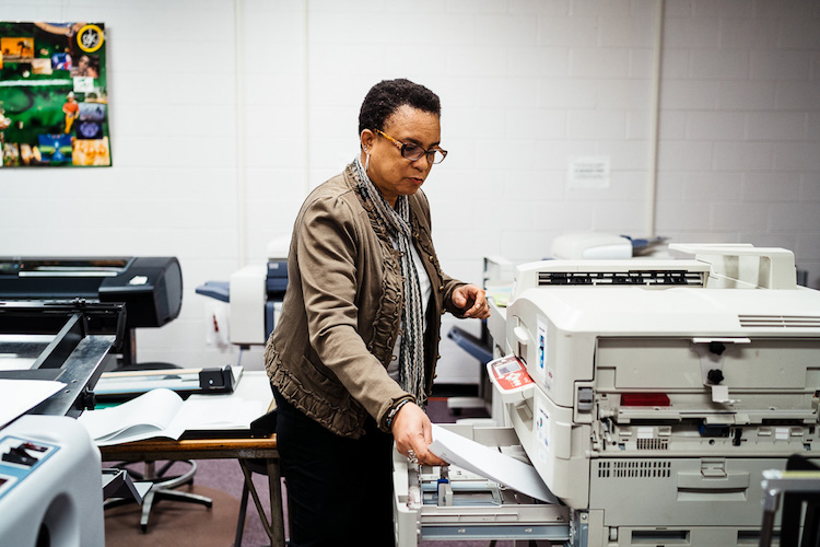 Leisia Duskin, Special Instructor for Graphics and Printing Technology classes, loading paper into the large capacity color printer
