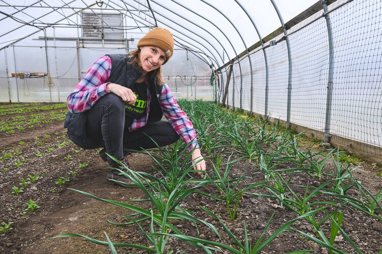 Jae Gerhart, manager of the Farm at THAA, crouches next to plants growing in a greenhouse. 