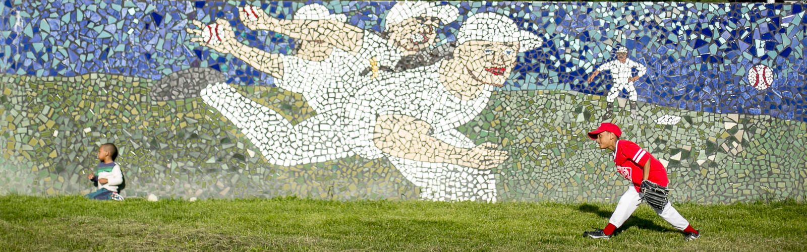 A child plays with a ball in front of a mosaic by artist Hubert Massey