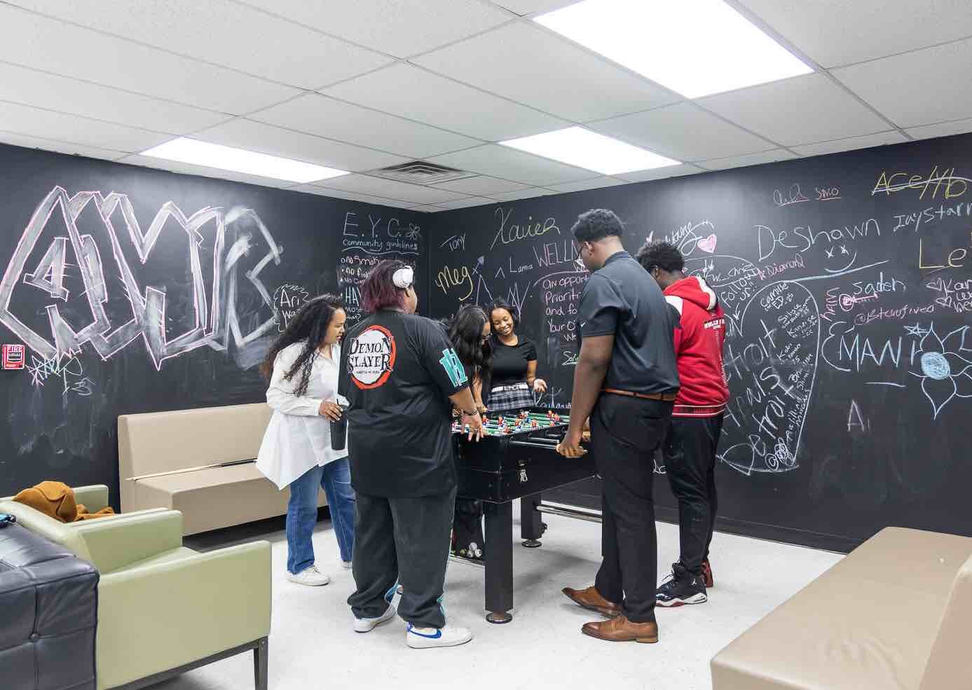 Caitlin Crutcher (white shirt) plays foosball with youth before programming at Eastside Community Network